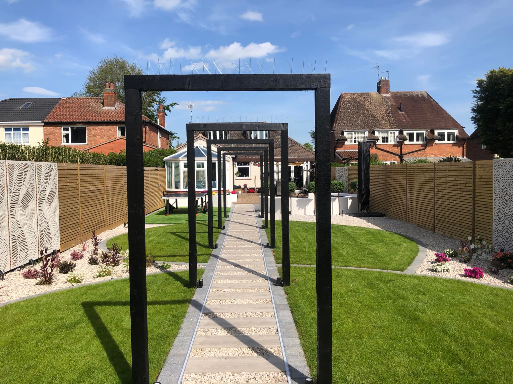 Black pergola arch walkway leading through circular lawn to conservatory, Evington Leicester